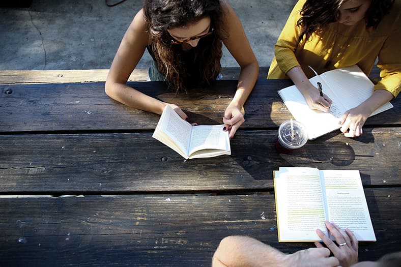 Jóvenes escribiendo en una mesa al aire libre.