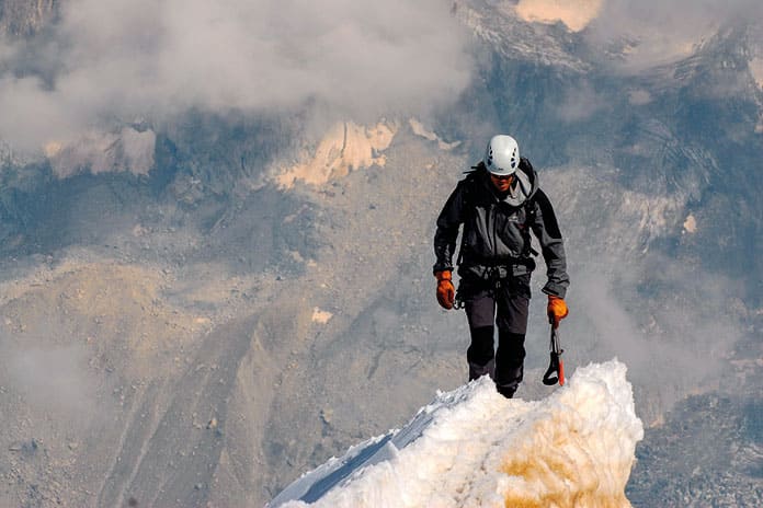 Montañero en la cima simboliza el esfuerzo espiritual de alcanzar la fortaleza desde la humildad.