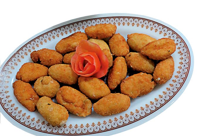 Fuente de croquetas de langostinos caseras recién fritas, acompañadas de ensalada mixta con lechuga, tomate y aceitunas negras