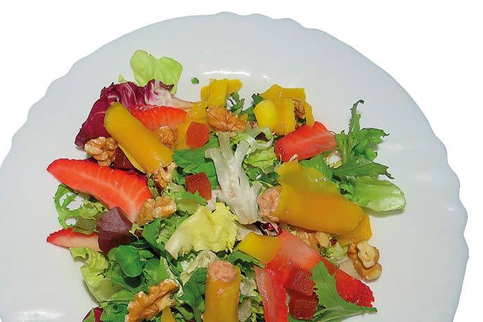 Primer plano de una ensalada de brotes tiernos con canutillos de mango rellenos de paté, nueces y fresas